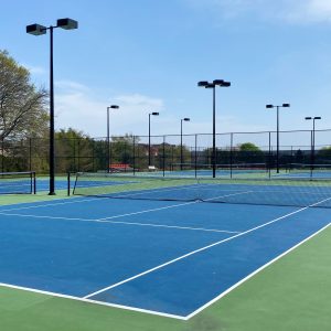 An empty tennis court with a blue and green surface and lights fenced in at a local school.