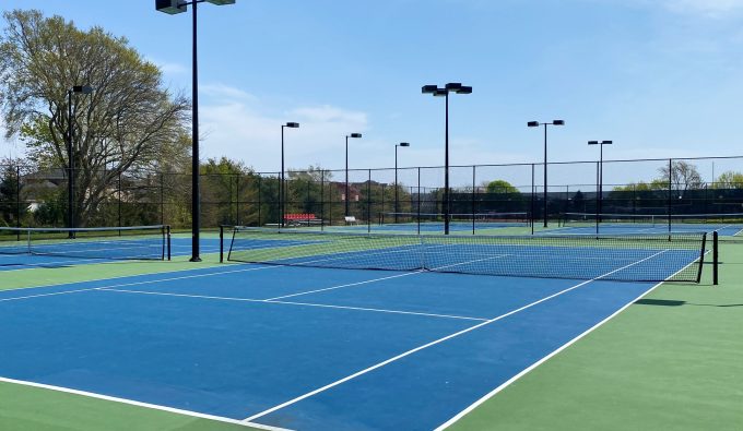 An empty tennis court with a blue and green surface and lights fenced in at a local school.