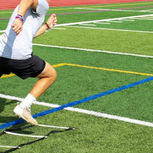 High school football player running though the ladder during summer sports camp on a turf field.