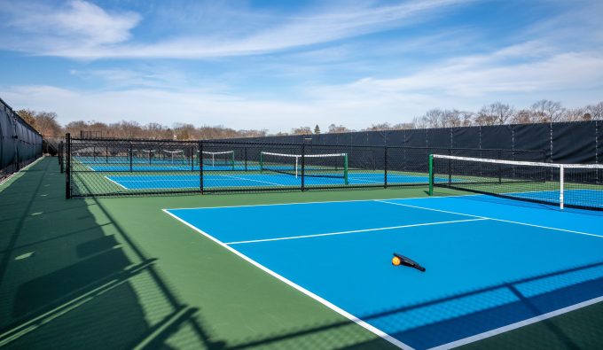 View of a new pickleball complex with a paddle and orange ball on blue and green courts in a suburban setting during early spring.